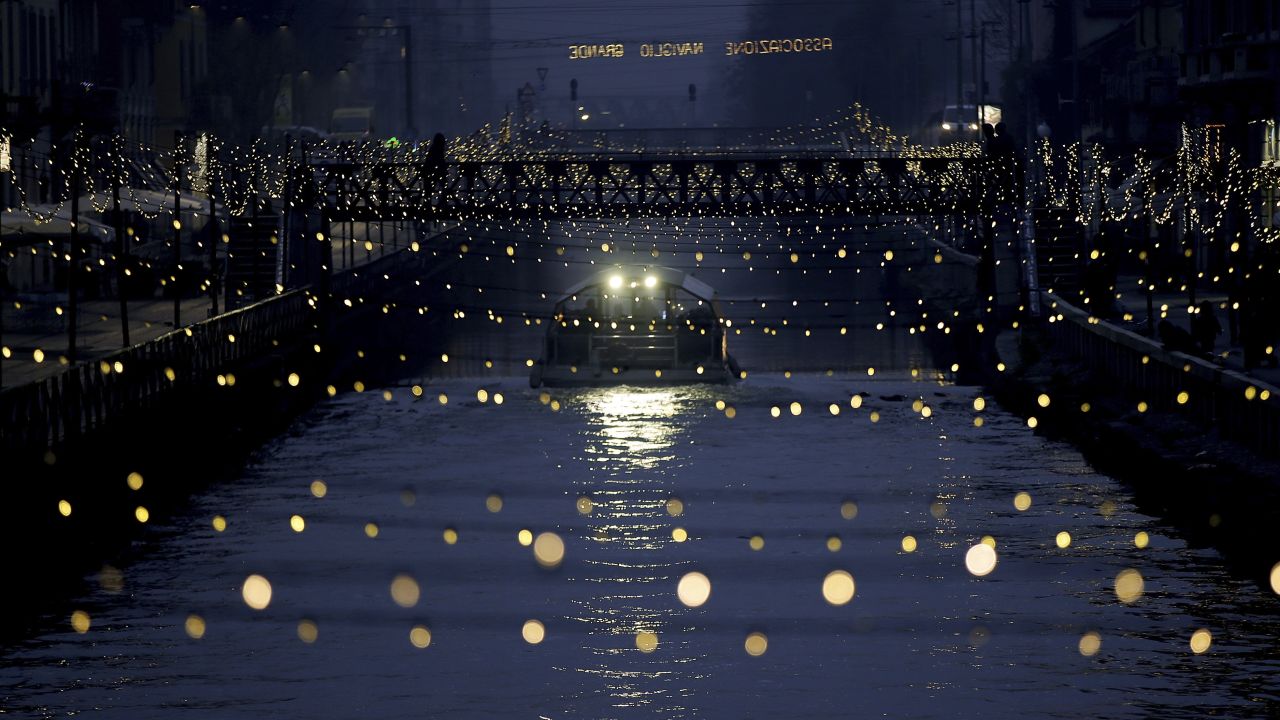A tourist boat sails beneath Christmas lights illuminating Darsena dei Navigli, a Milan neighborhood named for the canals that run through it. 