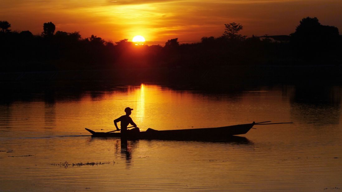 As the sun sets in Naypyitaw, Myanmar, a fisherman paddles his boat on a lake.