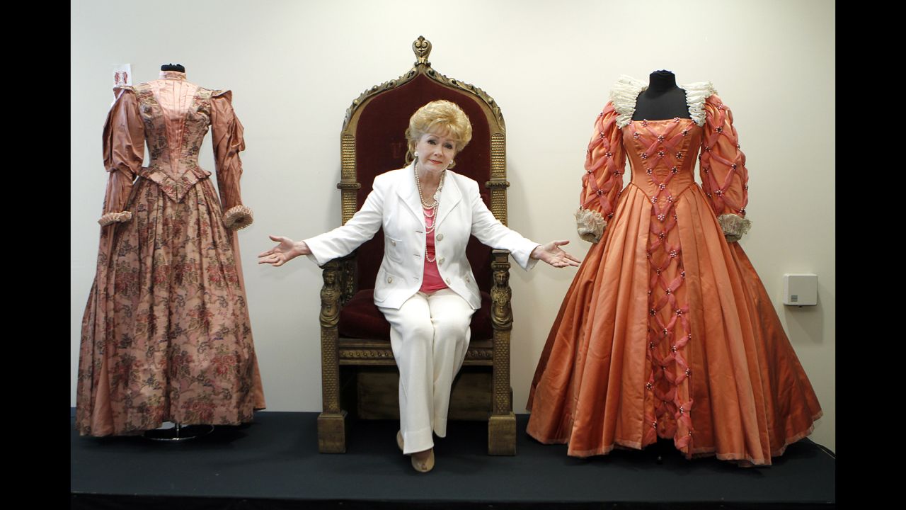 Reynolds poses before the auction of her massive collection of memorabilia from classic movies in 2011. Reynolds is siting on the throne from the 1955 movie "Virgin Queen" with a dress worn by Bette Davis, right, and Joan Collins, left.
