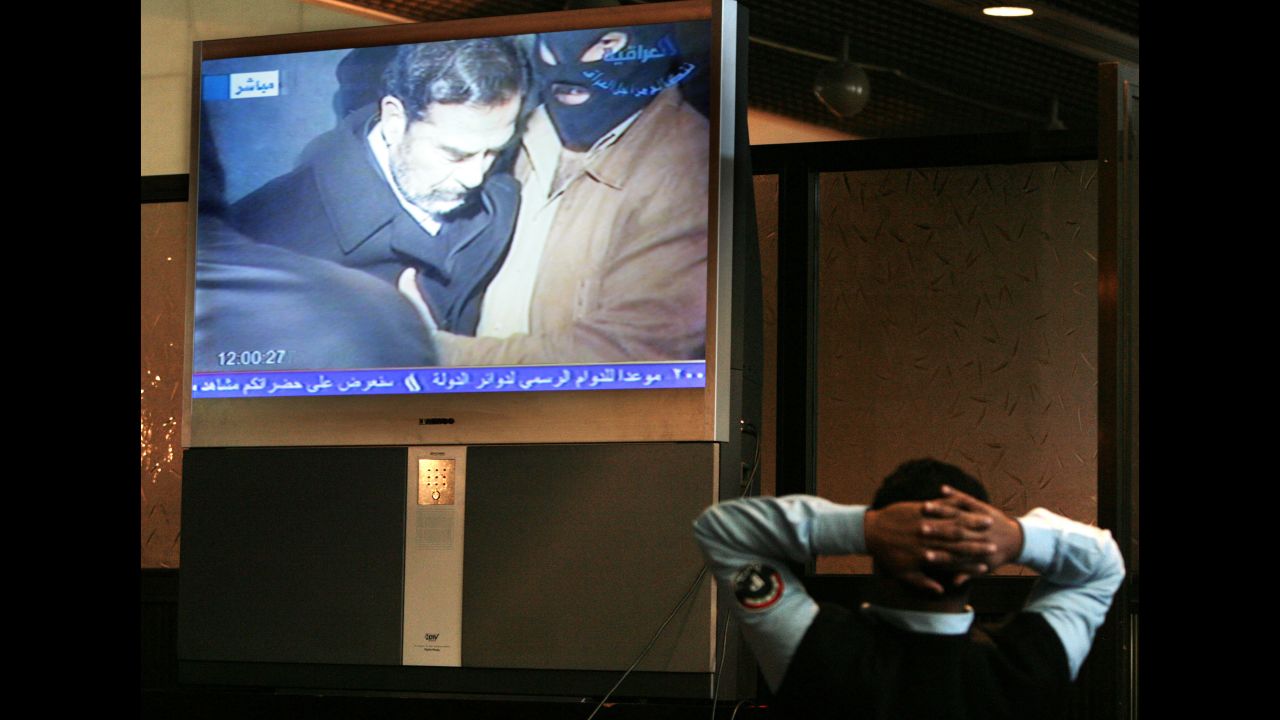 An Iraqi policeman watches a broadcast of Saddam Hussein moments before his execution.