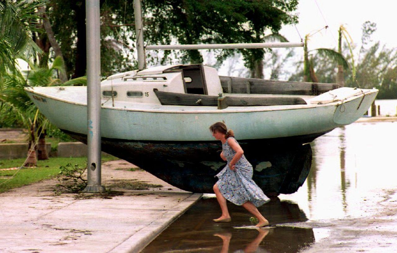 A woman jumps across a flooded street in Coconut Grove, Miami, on Aug 24, 1992, in front of a sailboat washed ashore by Hurricane Andrew. 