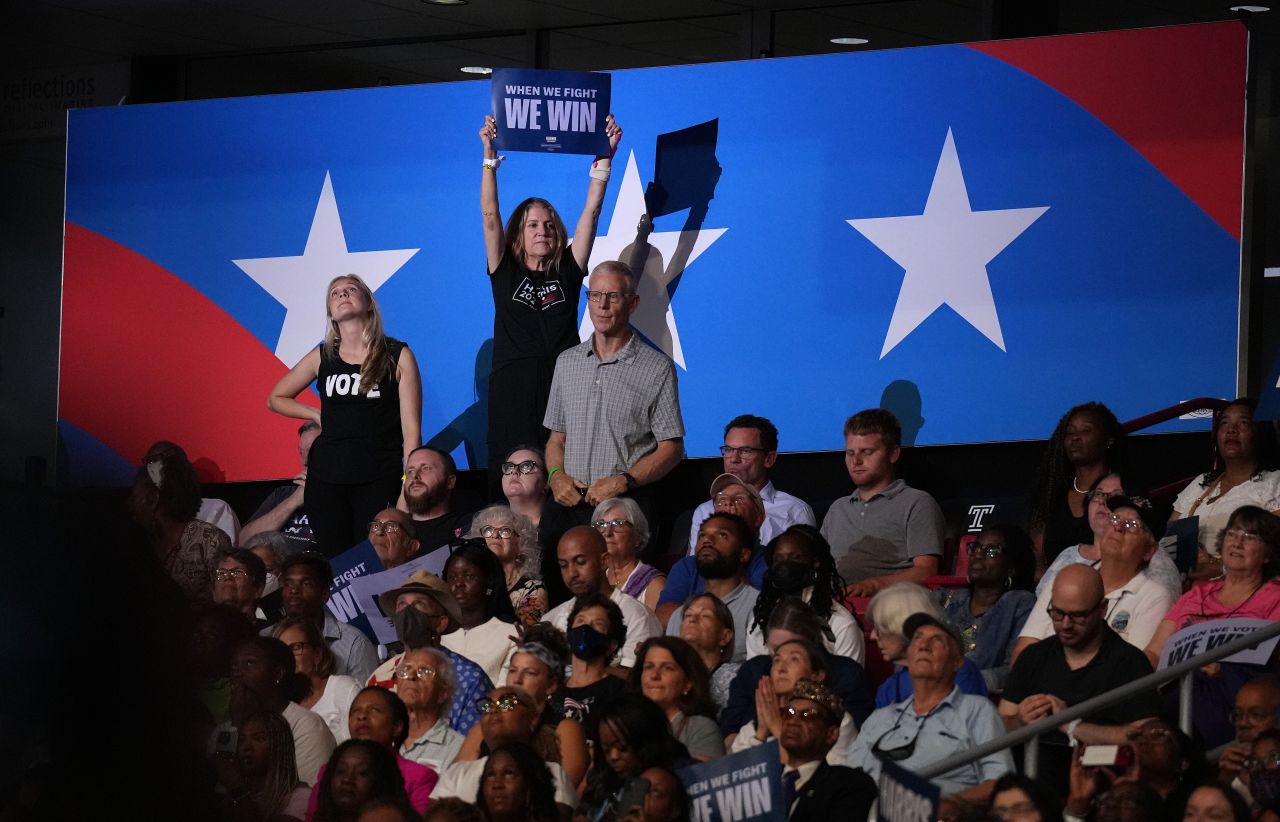 Supporters cheer and wave signs as Harris and Walz speak on stage.