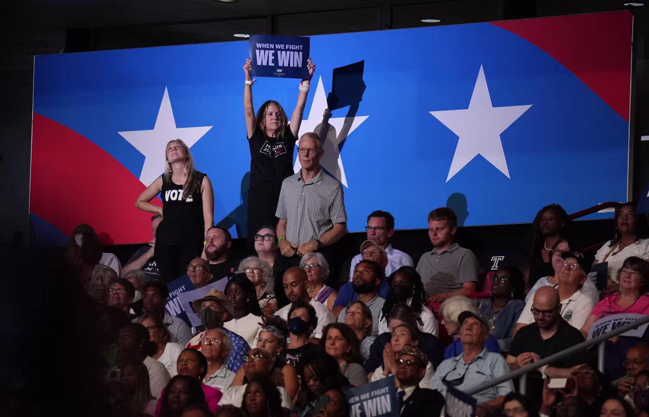 Supporters cheer and wave signs as Harris and Walz speak on stage.