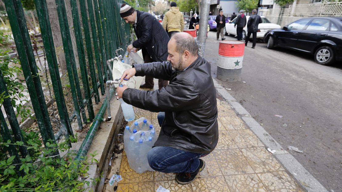 Damascus residents fill plastic containers with water at a public fountain.