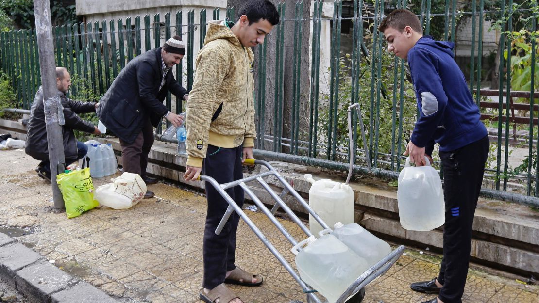 Syrians fill plastic containers with water at a public fountain by a park in Damascus.