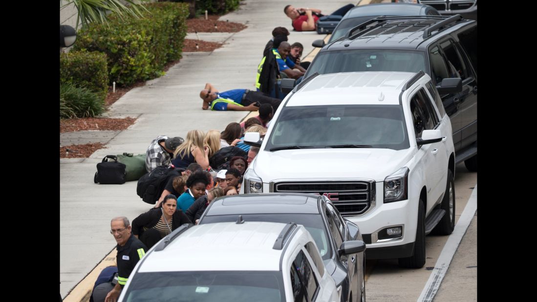 People take cover outside the airport in the chaos following the shooting.