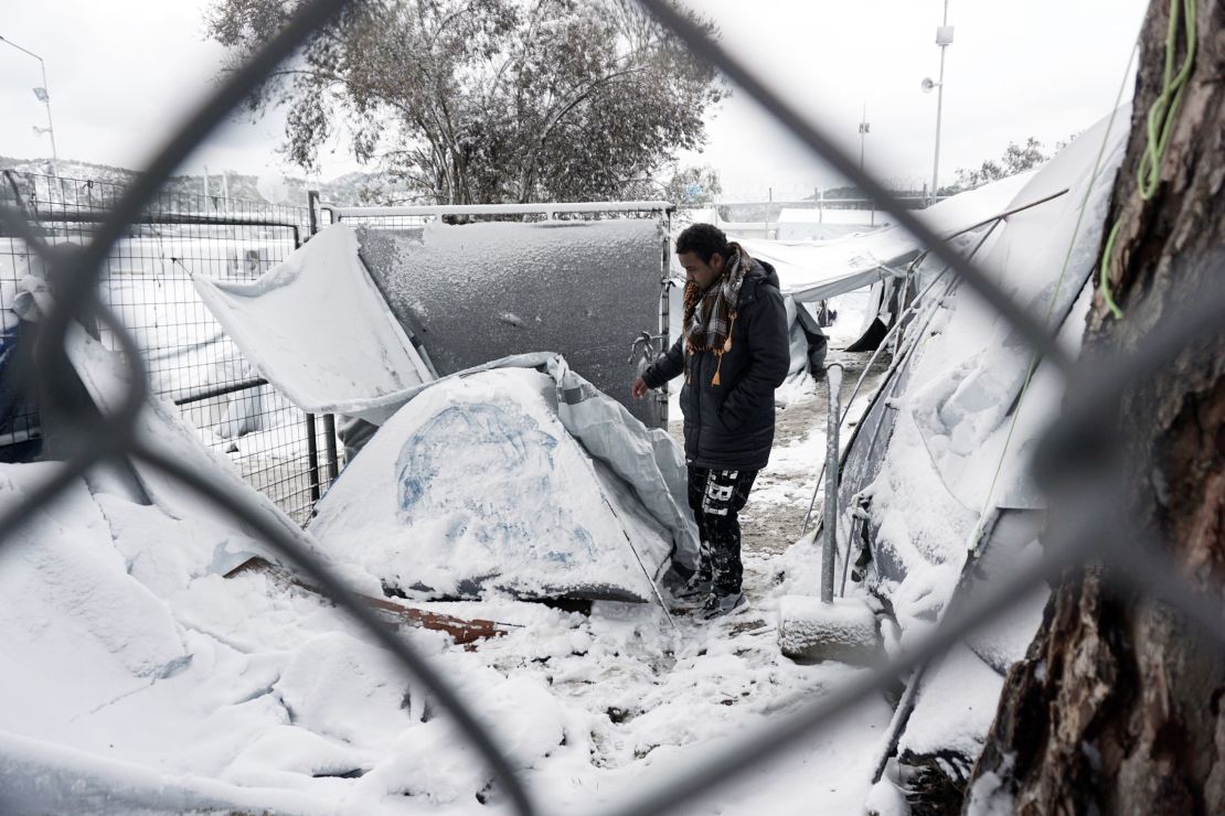 A migrant stands next to a snow-covered tent at the Moria refugee camp, Lesbos.