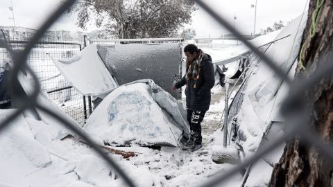 A migrant stands next to a snow-covered tent at the Moria refugee camp, Lesbos.