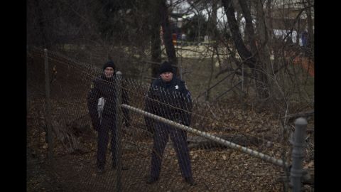 Police officers watch from behind a fence.