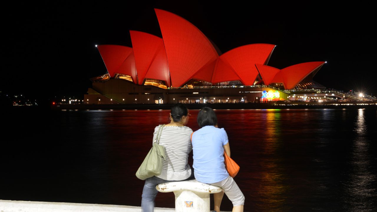 Chinese tourists view the Sydney Opera House which is lit up red to welcome in the Lunar New Year of the Monkey in Sydney on February 8, 2016. 