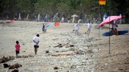 Foreign tourists and locals alike walk along the popular Kuta beach covered with debris and rubbish washed up by the tide, near Denpasar on the resort island of Bali. 