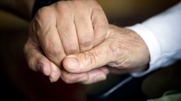 An elderly man holds the hand of his carer in an old people's home in Berlin, October 2013. 