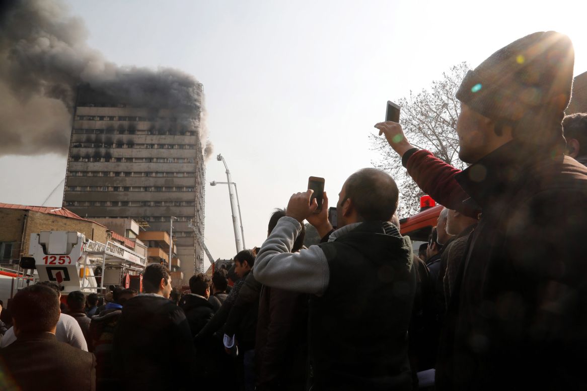 Residents take photos of the Plasco building engulfed in smoke and flames.