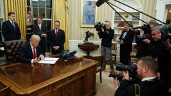 President Donald Trump signs his first executive order in the Oval Office of the White House on January 20, 2017.