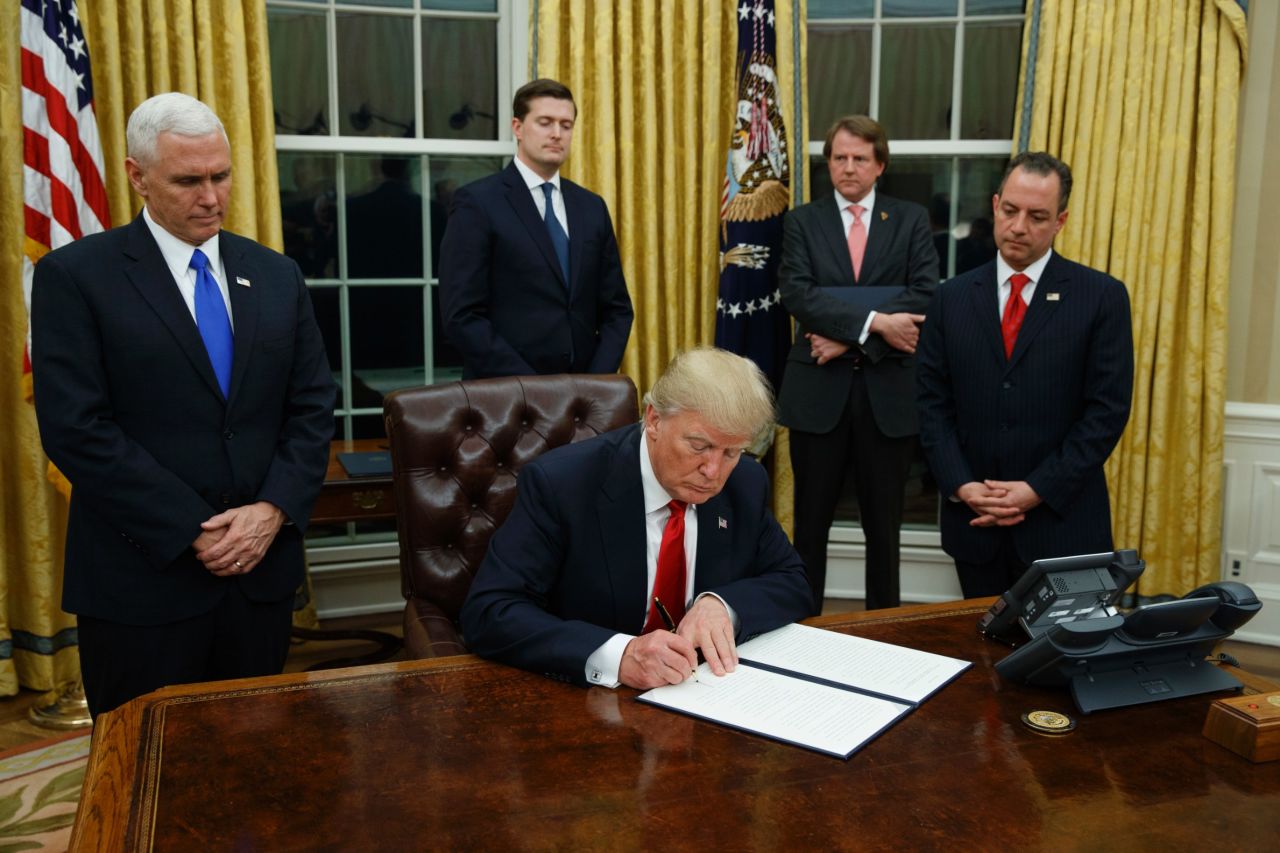 President Donald Trump, flanked by Vice President Mike Pence and Chief of Staff Reince Priebus, signs his first executive order on health care, Friday, January 20, in the Oval Office of the White House in Washington.