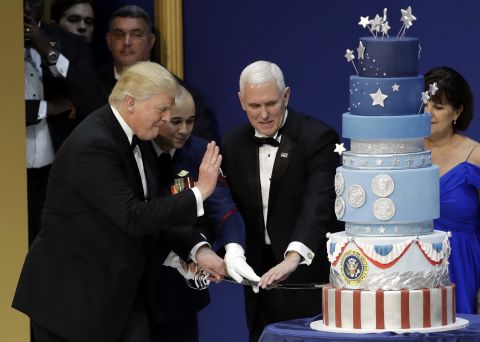 President Donald J. Trump, left, and Vice-President Mike Pence, right, are helped by Coast Guard Petty Officer 2nd Class Matthew Babot, center, as they cut a cake at The Salute To Our Armed Services Inaugural Ball.