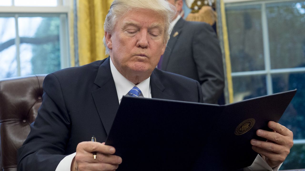 President Donald Trump reads an executive order withdrawing the US from the Trans-Pacific Partnership prior to signing it in the Oval Office of the White House in Washington, DC, January 23, 2017.