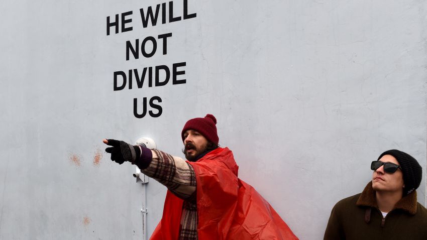 US actor Shia LaBeouf(L) during his He Will Not Divide Us livestream outside the Museum of the Moving Image in Astoria, in the Queens borough of New York January 24, 2017 as a protest against President Donald Trump.  
LaBeouf has installed a camera at the Museum of the Moving Image in New York that will run a continuous live stream for the duration of Trumps presidency. LaBeouf is inviting the public to participate in the project by saying the phrase, He will not divide us, into the camera. / AFP / TIMOTHY A. CLARY        (Photo credit should read TIMOTHY A. CLARY/AFP/Getty Images)