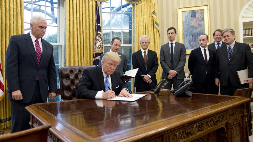 WASHINGTON, DC - JANUARY 23:  (AFP OUT) U.S. President Donald Trump signs the first of three Executive Orders in the Oval Office of the White House in Washington, DC on Monday, January 23, 2017.  They concerned the withdrawal of the United States from the Trans-Pacific Partnership (TPP), a US Government hiring freeze for all departments but the military, and "Mexico City" which bans federal funding of abortions overseas.  Standing behind the President, from left to right: US Vice President Mike Pence; White House Chief of Staff Reince Preibus; Peter Navarro, Director of the National Trade Council; Jared Kushner, Senior Advisor to the President; Steven Miller, Senior Advisor to the President; unknown; and Steve Bannon, White House Chief Strategist. (Photo by Ron Sachs - Pool/Getty Images)
