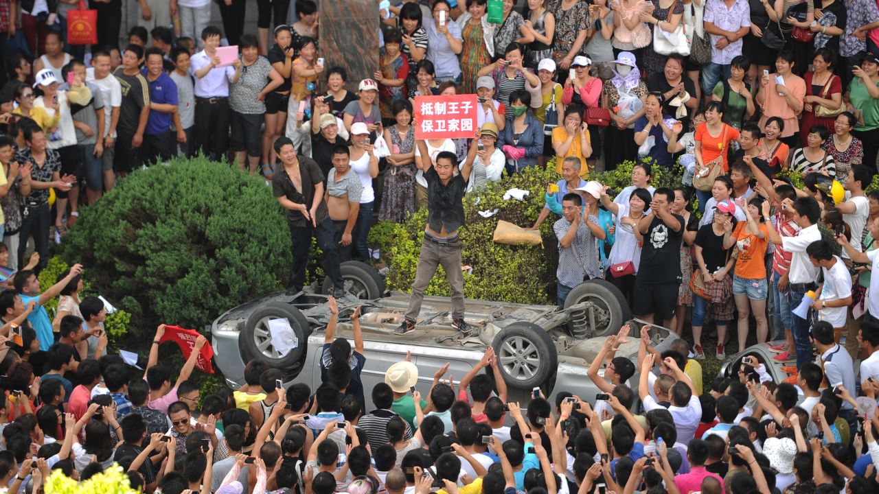A man holds a placard as he stands on a car overturned by a group of anti-pollution protestors on July 28, 2012.