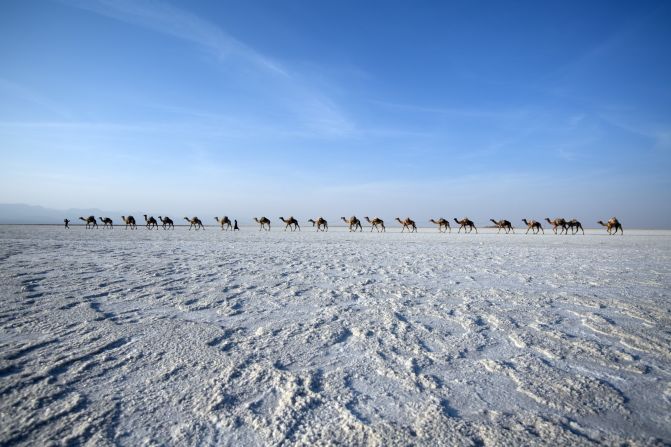 A camel caravan carries the riders' produce across a salt plain. <br /><br />A new road is being cut through the depression, which could reduce the animals' burden. 
