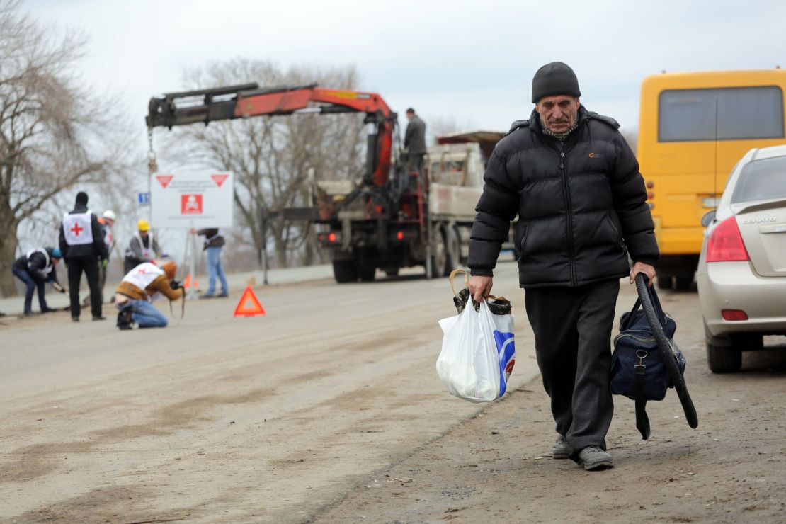 A local resident walks past Red Cross employees installing billboards reading "Danger! Mines! Do not leave the road!" near Berezove in Donetsk region in March 2016.