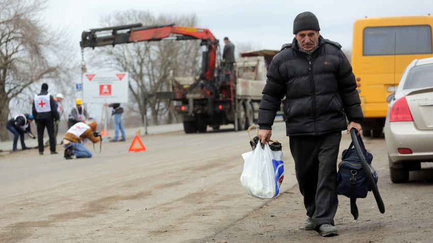 A local resident walks past Red Cross employees installing billboards reading "Danger! Mines! Do not leave the road!" near the Ukrainian village of Berezove, Donetsk region on March 28, 2016.