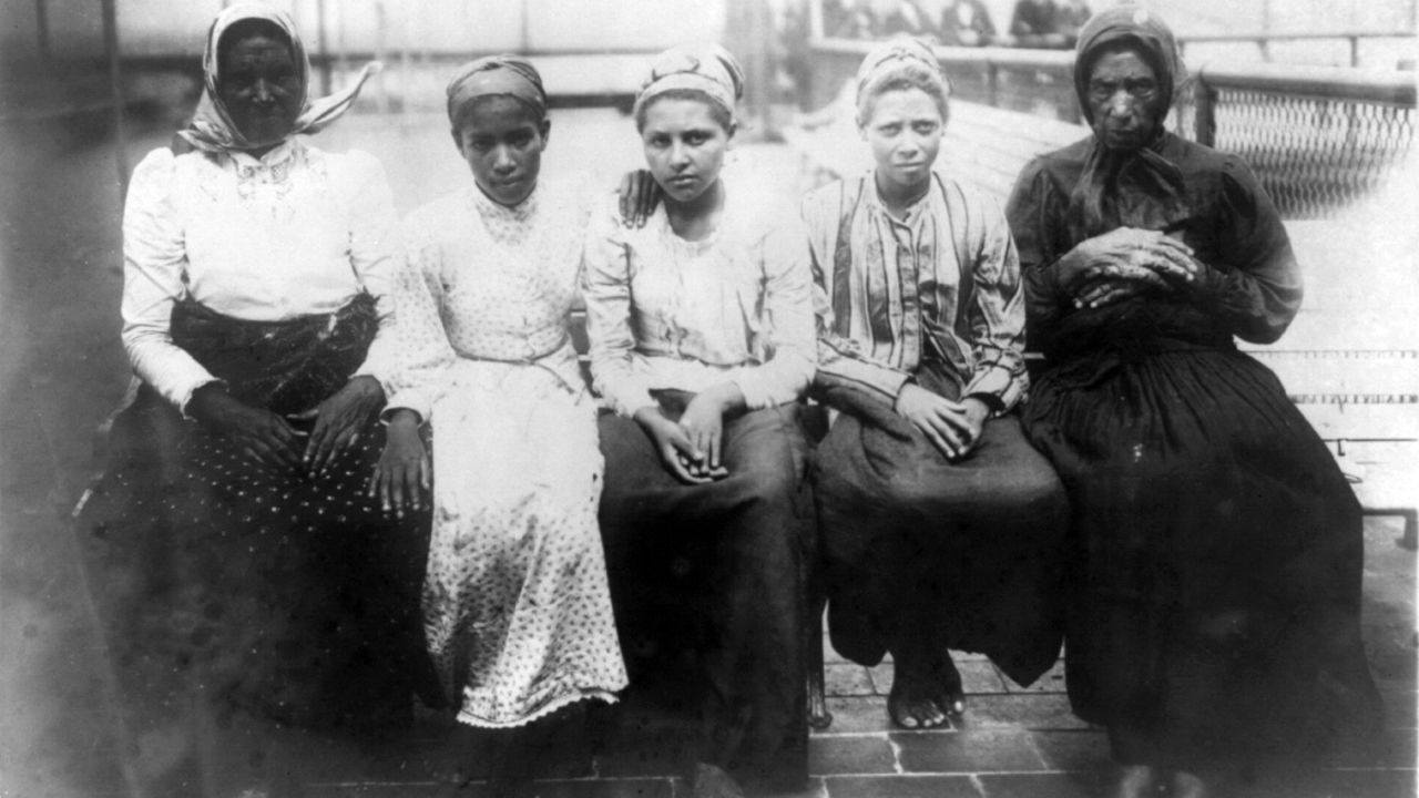 Five newly arrived immigrants sit on a dock at Ellis Island in 1910.