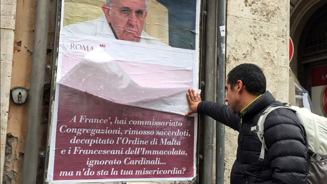 A passerby lifts a paper sheet covering an anti-Pope Francis poster in central Rome on Saturday.