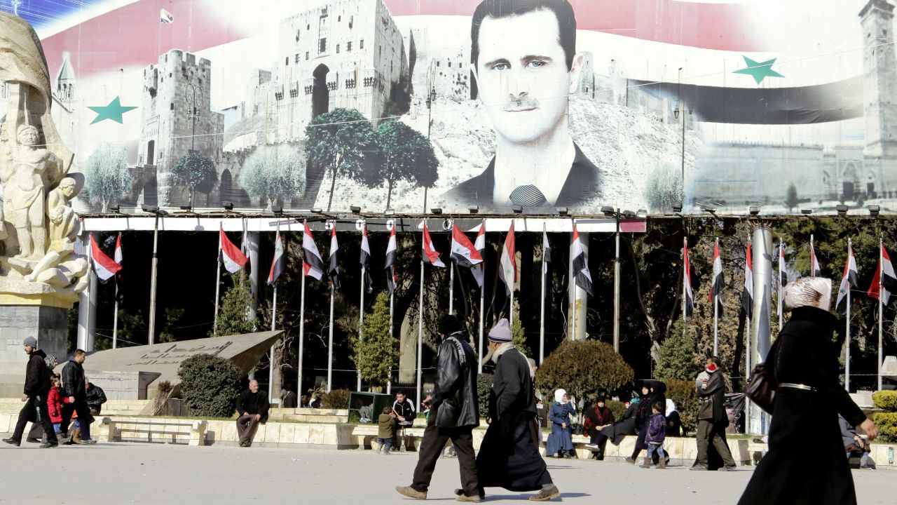 Syrians walk past a poster of President Assad in Aleppo.