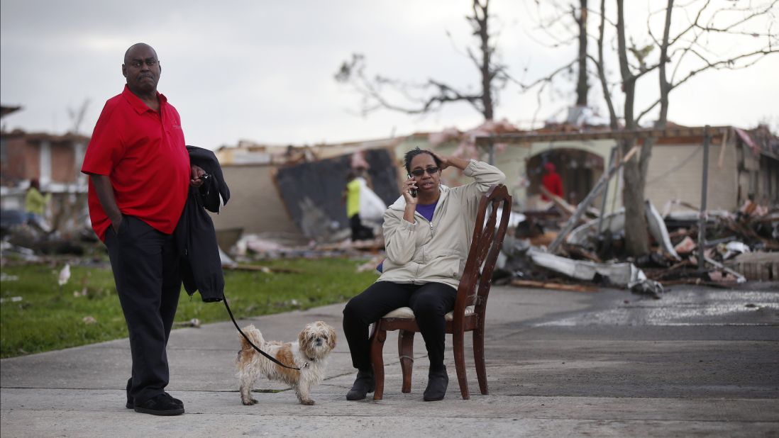 Across the street from her  destroyed home, Claire White sits in a chair and talks on the phone next to her husband, Roy, and dog JD.