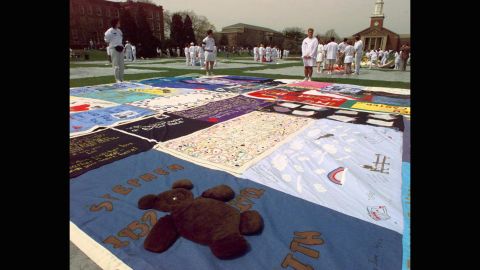 A teddy bear adorns one more than 400 panels of the AIDS Memorial Quilt as volunteers stand by silently during a 1996 ceremony at <strong>Elmhurst College</strong> in Elmhurst, Ilinois.  