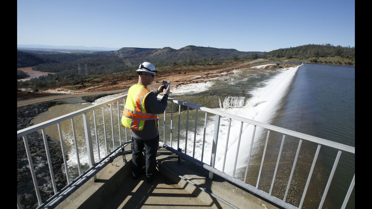 Jason Newton of the California Department of Water Resources photographs water flowing over the emergency spillway alongside the dam on Saturday, February 11.
