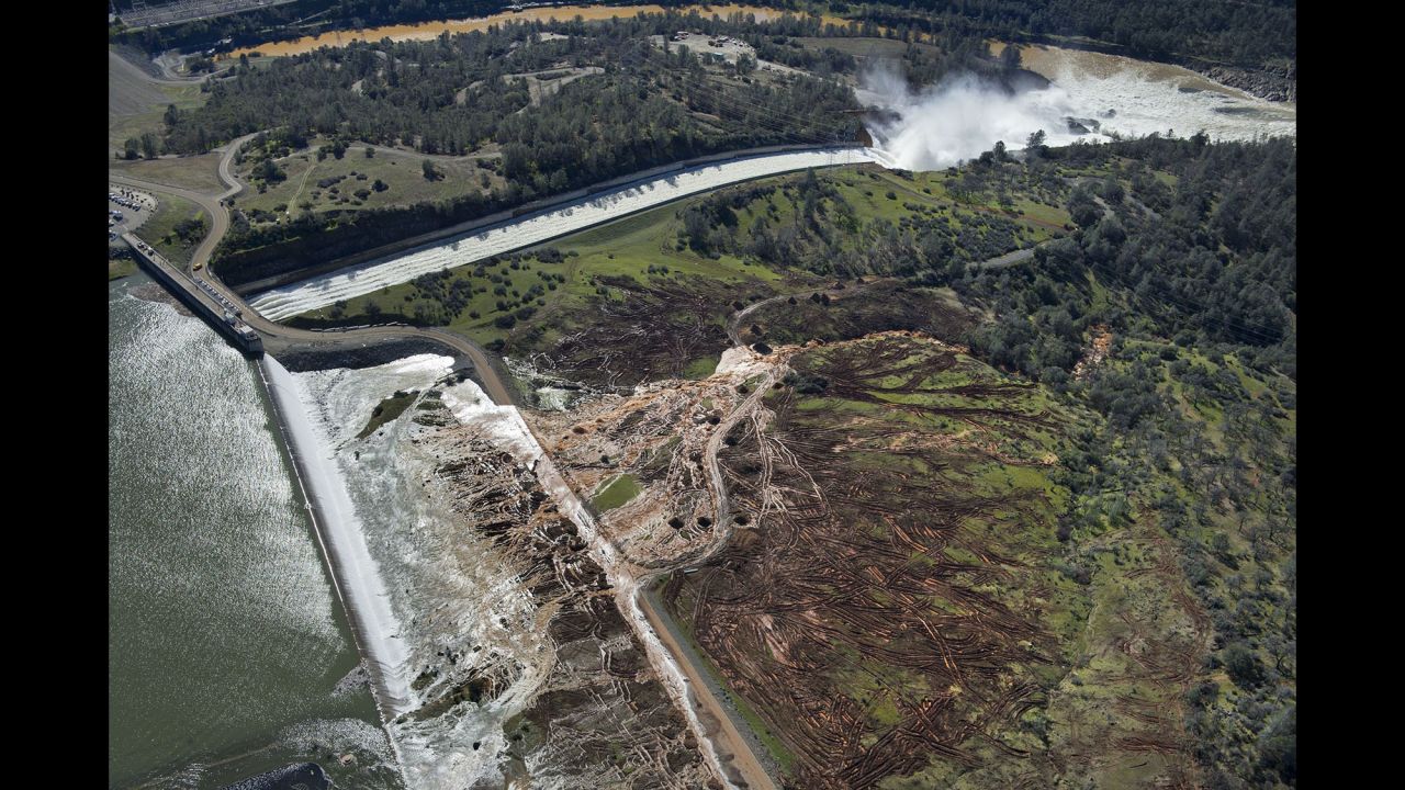 Water flows over an emergency spillway (bottom right) at Lake Oroville Dam on Saturday, February 11. The damage has affected both the primary and the emergency spillways, which serve as channels to drain water from the lake to prevent overflow.