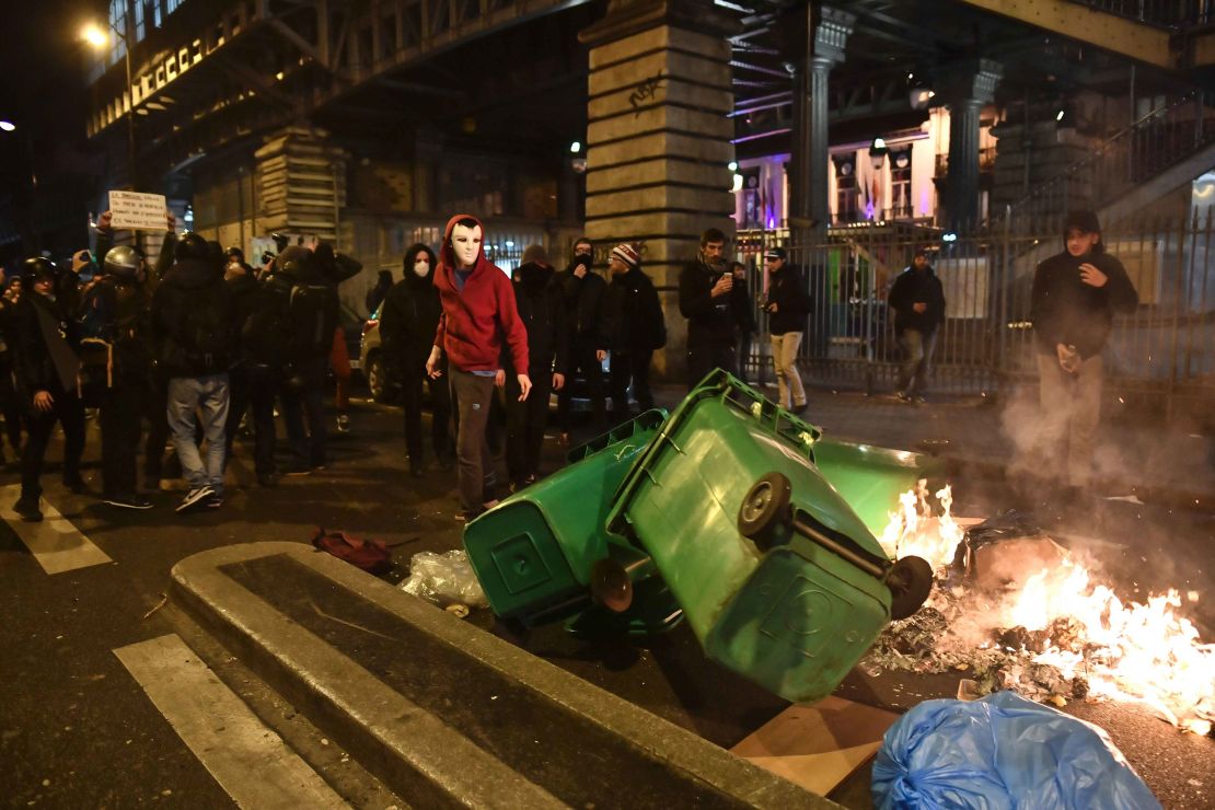 Protesters stand in front of burning trash bins.