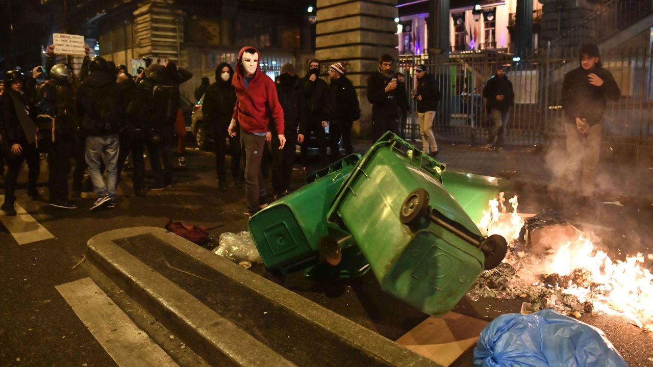 Protesters stand in front of burning trash bins.