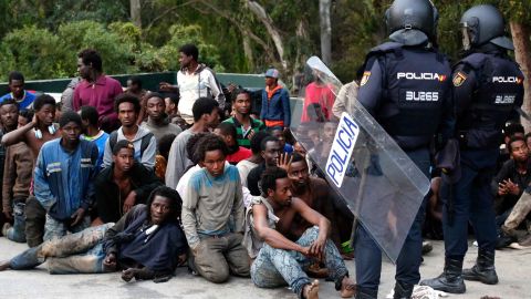 Migrants sit on the ground next to Spanish police officers after crossing into Ceuta.