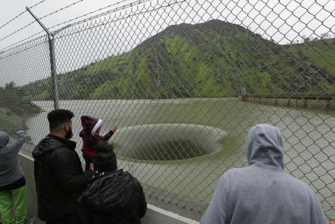 People stop to watch water flow into the iconic Glory Hole spillway at the Monticello Dam on February 20, in Lake Berryessa.  This is the first time in over a decade that water has been high enough to flow into  the 72-foot diameter spillway. 