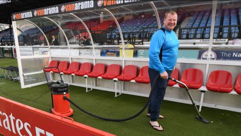 Wayne Shaw vacuums Arsenal's dugout before the match between Sutton United's game Monday. 