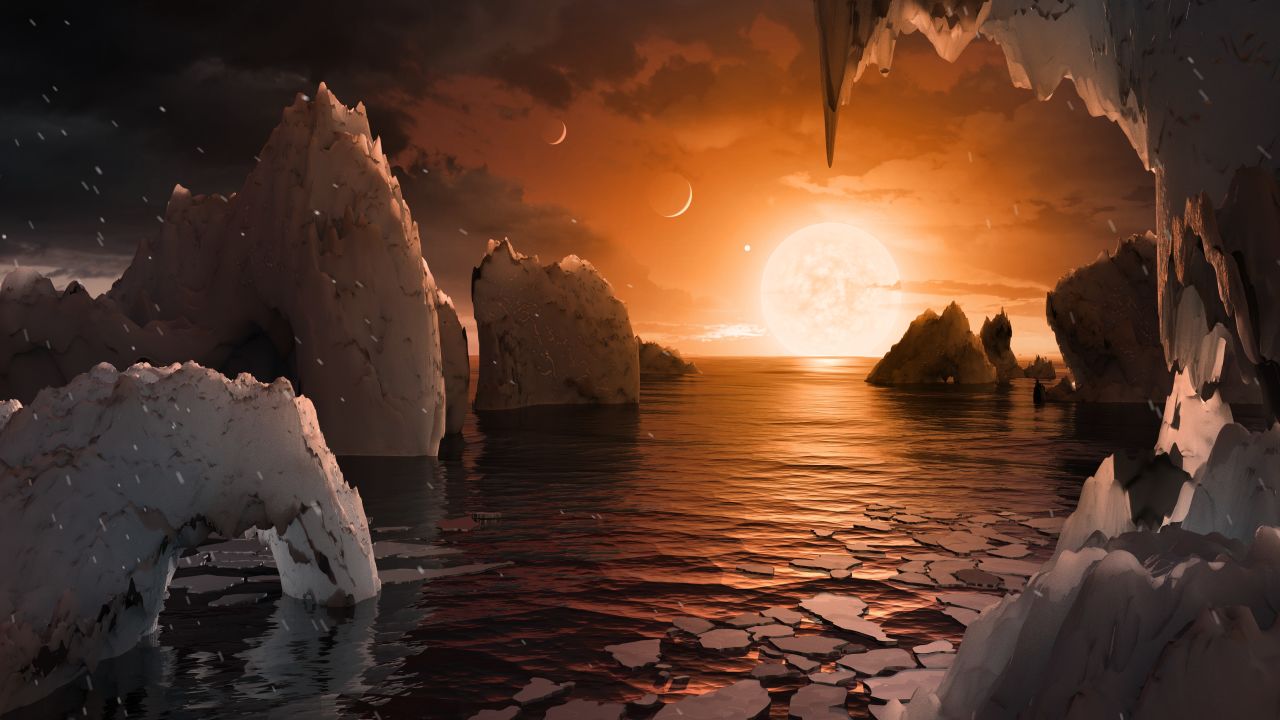 An artist's concept image of the surface of the exoplanet TRAPPIST-1f. Of the seven exoplanets discovered orbiting the ultracool dwarf star TRAPPIST-1, this one may be the most suitable for life. It is similar in size to Earth, is a little cooler than Earth's temperature and is in the habitable zone of the star, meaning liquid water (and even oceans) could be on the surface. The proximity of the star gives the sky a salmon hue, and the other planets are so close that they appear in the sky, much like our own moon.