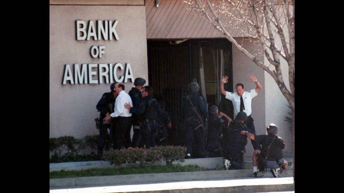 A bank employee holds up his hands as police search for more robbery suspects inside the bank.