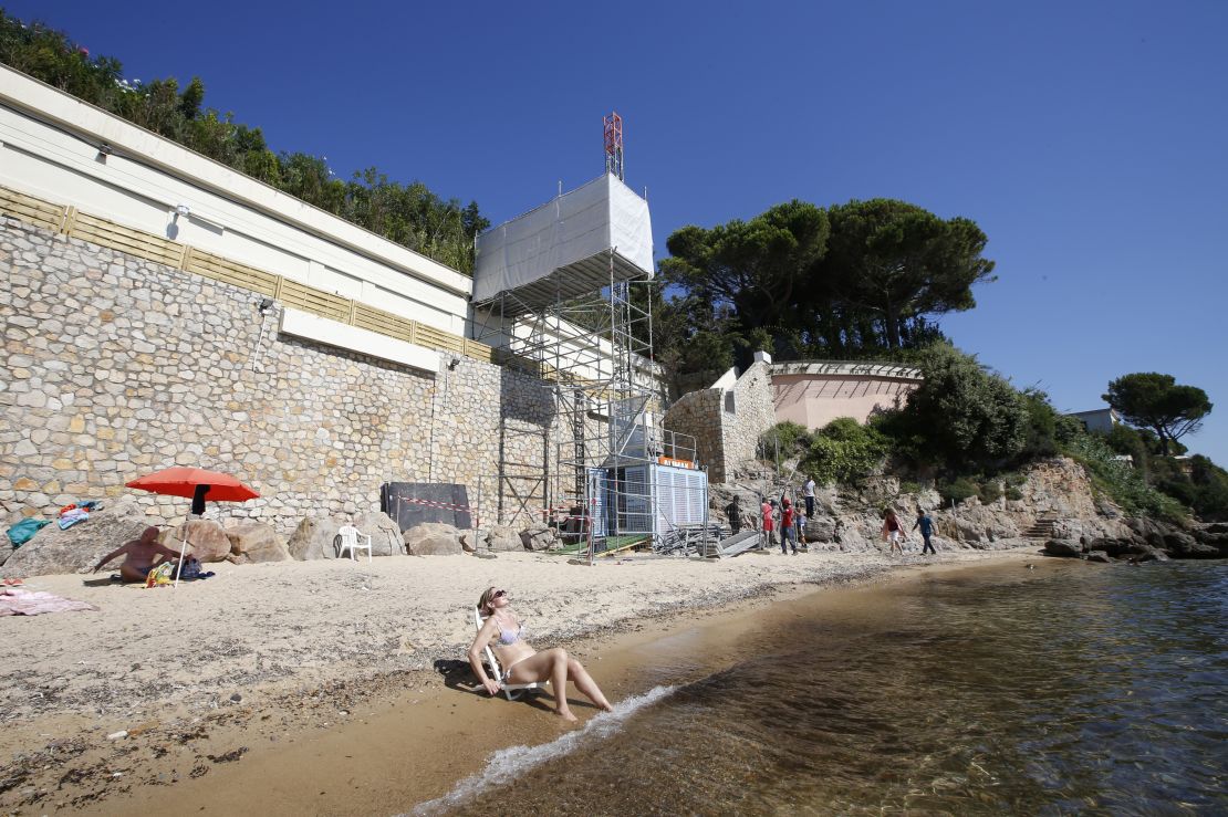 People sit and stand by the water as workers disassemble an elevator on the public beach near the Saudi King's villa in the Golfe-Juan seaside resort in Vallauris, southeastern France, on August 3, 2015. 