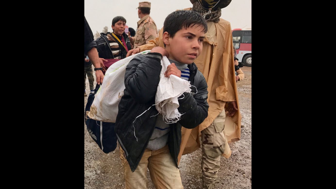 A young Iraqi boy carries a bag on his back as he walks in the rain to a civilian processing station south of Mosul. Some civilians have made the dangerous escape on foot from western Mosul.