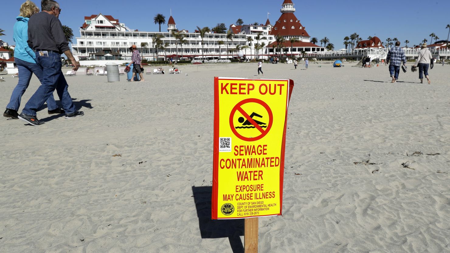 A sign warns of sewage contaminated ocean waters on a beach in front of the iconic Hotel del Coronado in Coronado, California. 