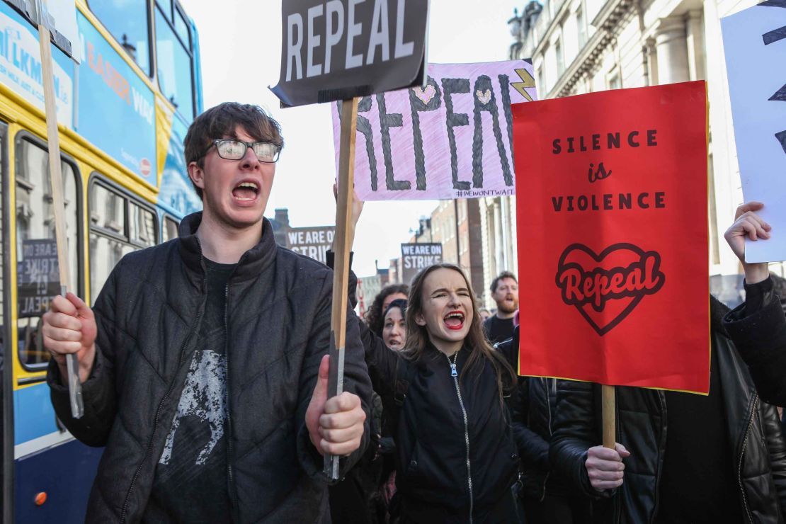 Signs reading "Silence is violence" and "Repeal" in the crowd.