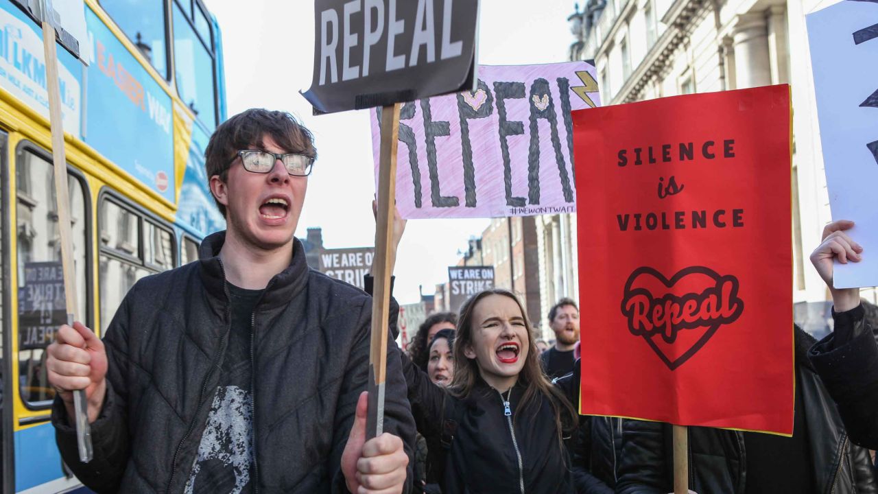 Signs reading "Silence is violence" and "Repeal" in the crowd.