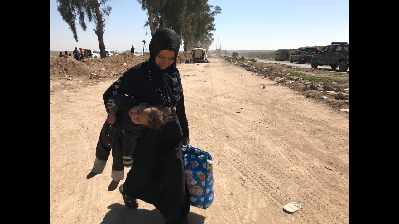 A woman carries her child in one hand and a bag of belongings in the other as she flees western Mosul's Mahata neighborhood. Many civilians are able to grab only a few belongings as they flee ISIS control.