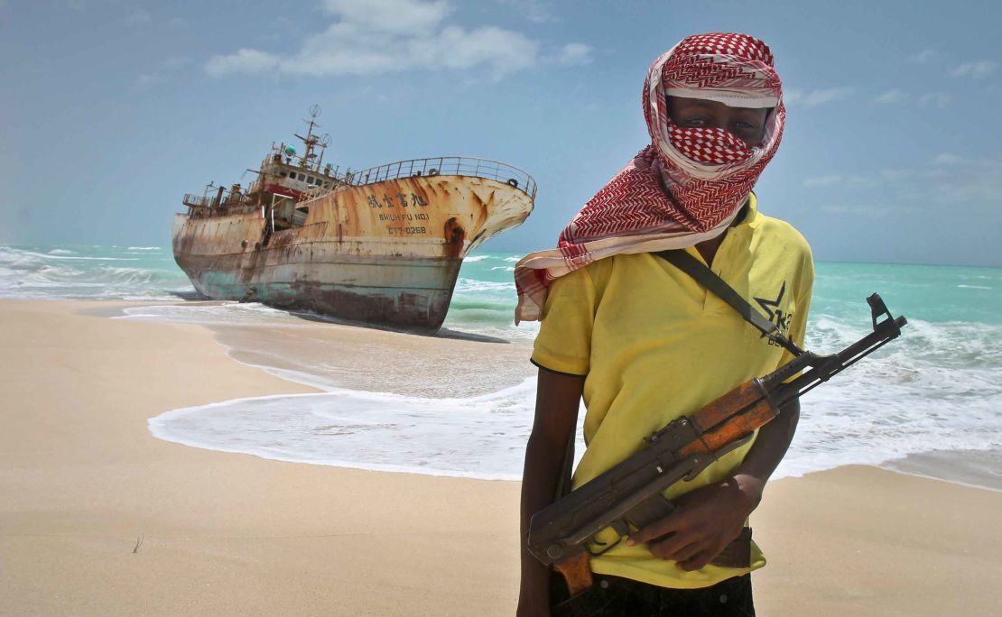 A masked and armed Somali pirate stands near a fishing vessel washed ashore. (AP Photo/Farah Abdi Warsameh)