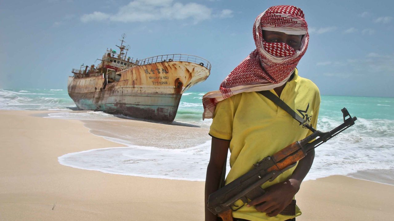 A masked and armed Somali pirate stands near a fishing vessel washed ashore. (AP Photo/Farah Abdi Warsameh)