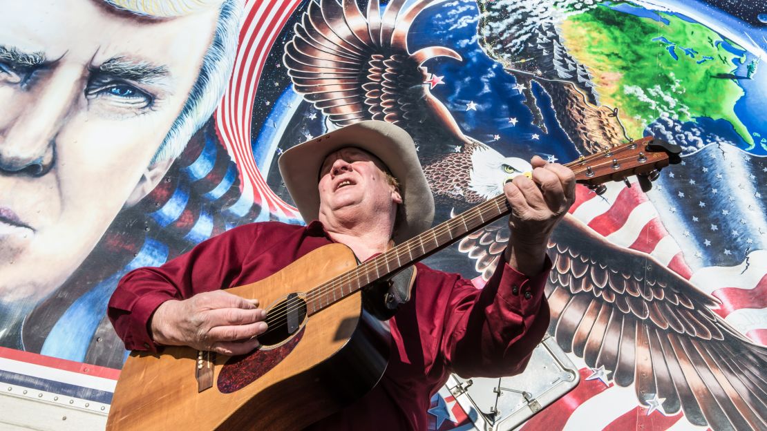 Kraig Moss, a supporter of Donald Trump during the campaign, sings a song outside a truck with a Trump painting last year in Iowa. Now, he regrets doing so.